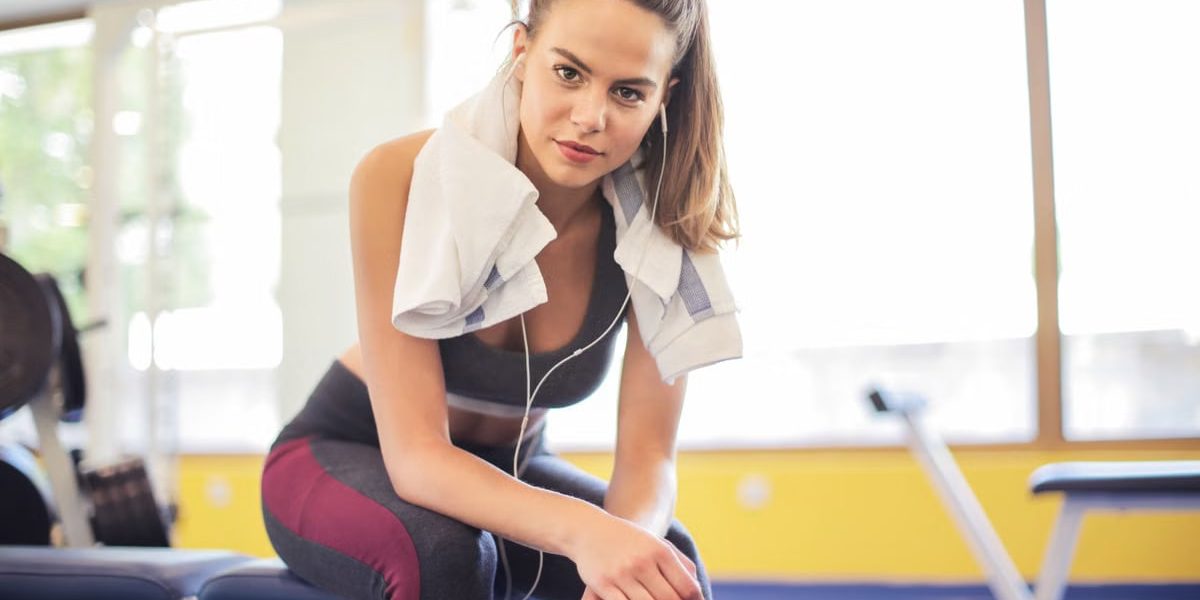A fit woman in activewear rests on a bench between workouts at the gym.